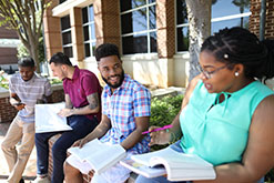 Students sitting in front of building sharing study notes.